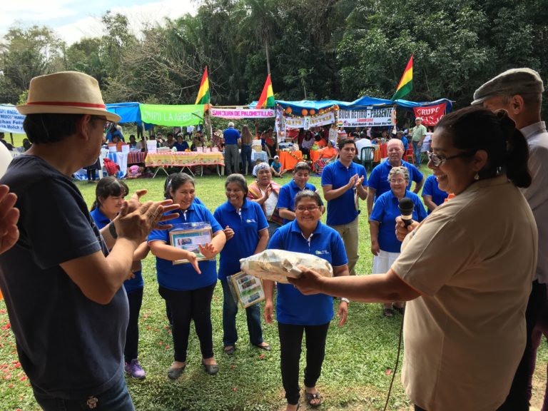 People gathered on a lawn, with community booths and Bolivian flags behind them